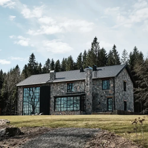 Moderne villa i natursten med store sorte sprossevinduer og skov som baggrund.
