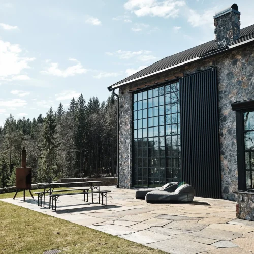 Moderne hus med naturstensfacade, store sprossevinduer og stenterrasse med udsigt til skoven.
